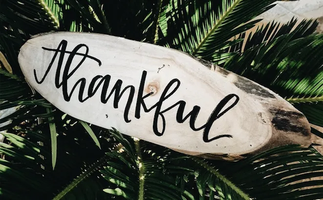 the word “Thankful” written in calligraphy style on a piece of wood