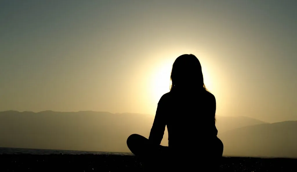silhouette of a woman meditating at sunset, with mountains in the background