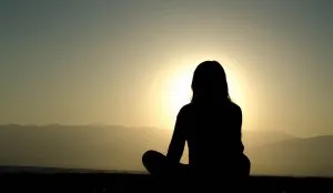 silhouette of a woman meditating at sunset, with mountains in the background